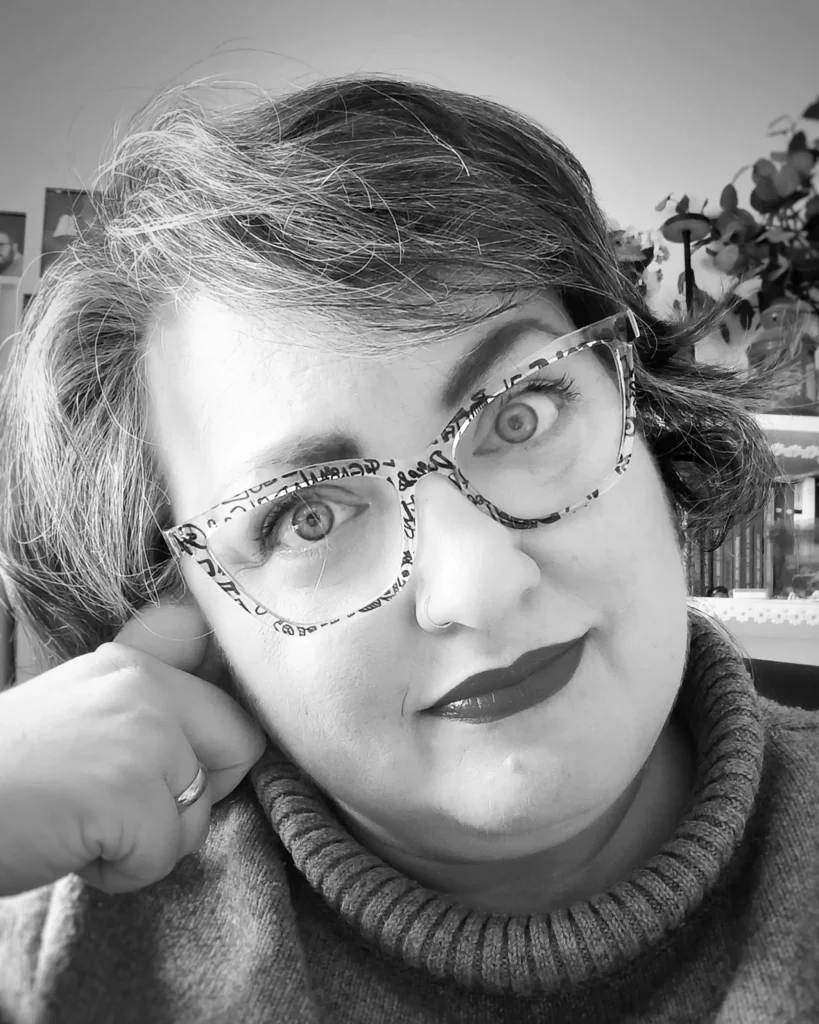 Ritratto in bianco e nero, di Margherita di 'Petali di Margherita': indossa occhiali cat-eye decorati e rossetto scuro, in un'atmosfera accogliente e professionale.