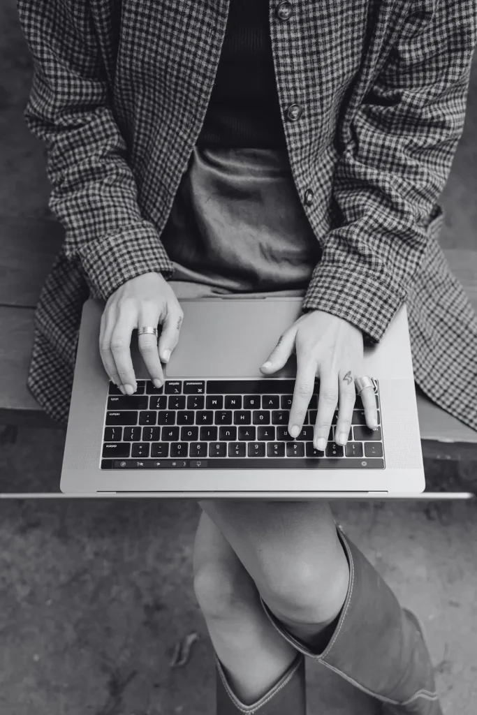 Una donna che scrive al computer portatile mentre è seduta su una panchina di legno all’aperto