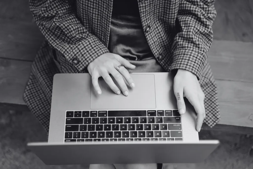 Una donna che scrive al computer portatile mentre è seduta su una panchina di legno all’aperto