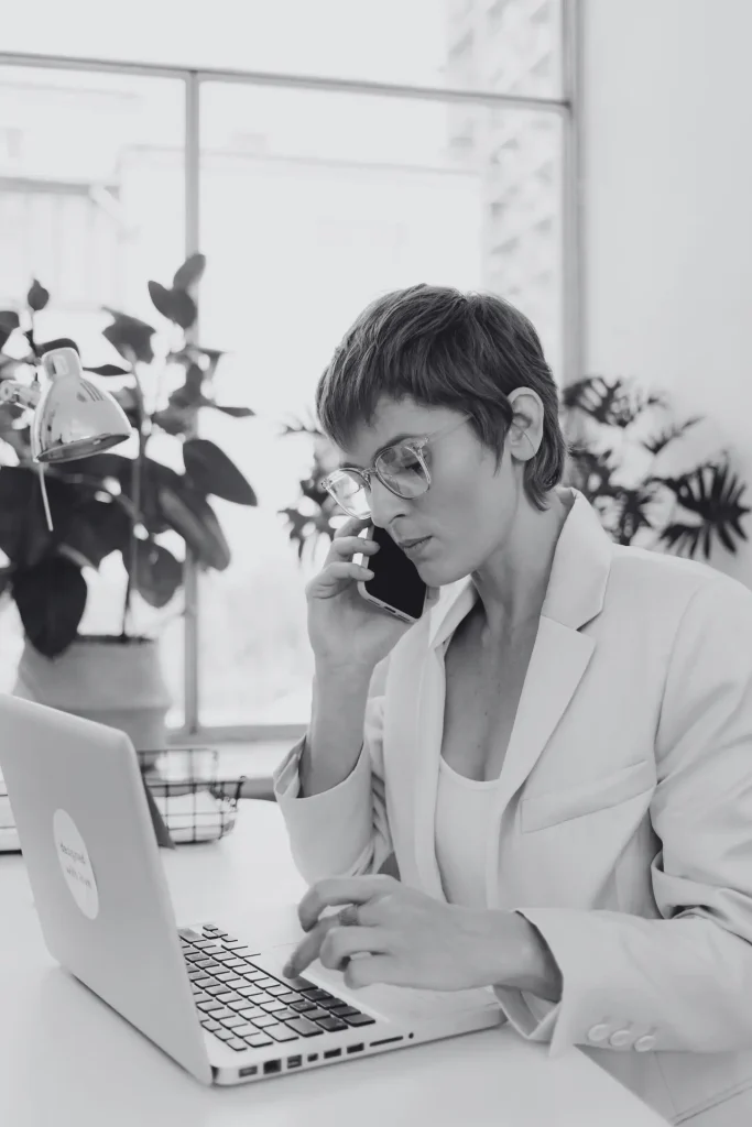 Una donna in carriera impegnata in più attività contemporaneamente con un portatile e un telefono in un ambiente d’ufficio moderno