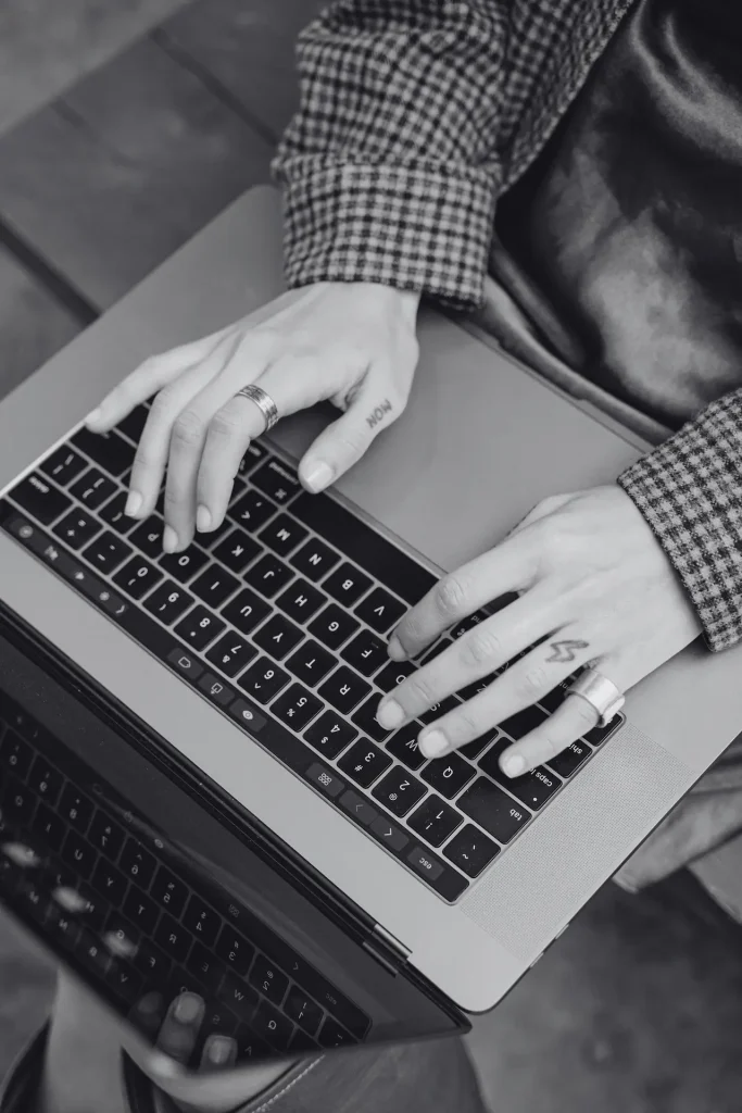 Un primo piano che ritrae delle mani tatuate intente a digitare su un portatile, mettendo in risalto la tecnologia moderna e lo stile personale
